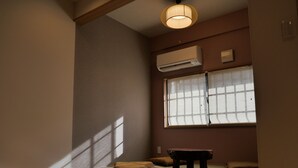 A room with a sloped ceiling, a window with blinds, a wooden bench, and a small table.
