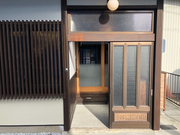 Une entrée de style japonais traditionnel, avec des portes coulissantes, une clôture en bois et un petit espace de véranda.