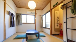 Ein Raum mit Tatami-Matten, einem niedrigen Tisch, Kissen, einer hängenden Matte und einer Schiebetür.