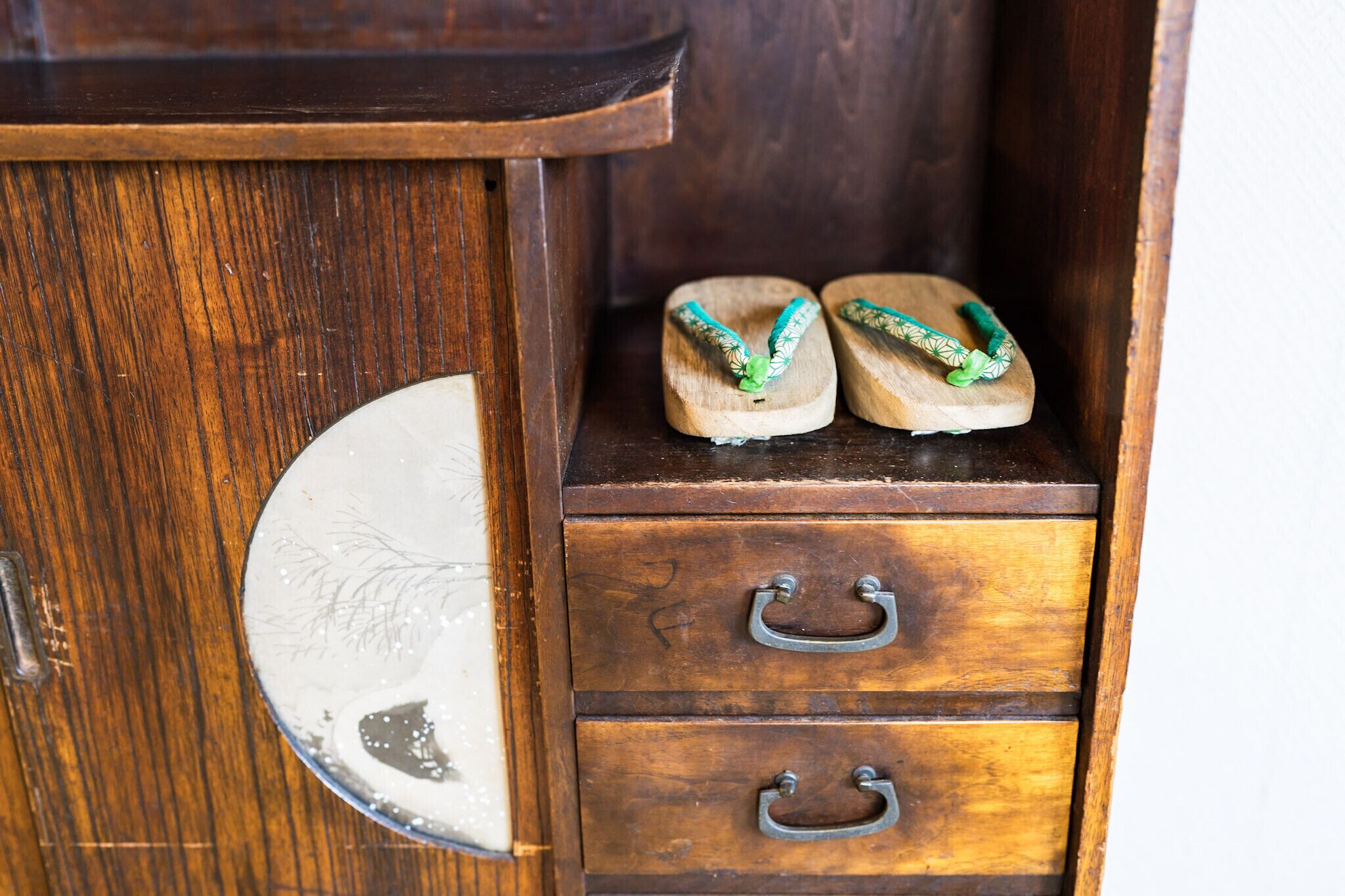 A wooden cabinet with two drawers and a round mirror.