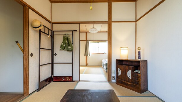 Ein traditioneller japanischer Raum mit Tatami-Boden, einer Schiebetür, einem Regal mit Dekoration und einem aufgehängten Hut.