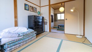 Ein traditioneller japanischer Raum mit Tatami-Boden, einem niedrigen Holzbett, einem schwarzen Schminktisch und einer hängenden Lampe.