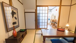 Ein traditioneller japanischer Raum mit Tatami-Boden, einem niedrigen Tisch, einem Holzkabinett und einer verschiebbaren Tür zu einem anderen Raum.