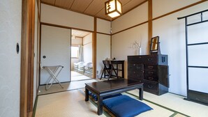 Ein traditioneller japanischer Raum mit Tatami-Boden, einem niedrigen Holztisch, einem dunklen Holzschrank und einer Hängeleuchte.