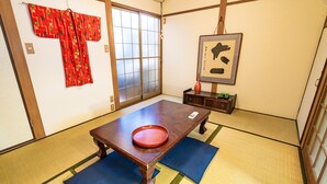 Ein traditioneller japanischer Raum mit Tatami-Bodenbelag, einem Holztisch mit roter Ablage und einer Schiebetür.