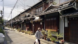 Eine traditionelle japanische Straße mit Holzhäusern, Topfpflanzen und einer Person, die geht.