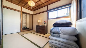 A traditional Japanese room with tatami flooring, a shoji screen, a wooden dresser, and a stack of futons.