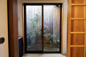 A sliding glass door leading to a garden with a wooden fence and various plants.
