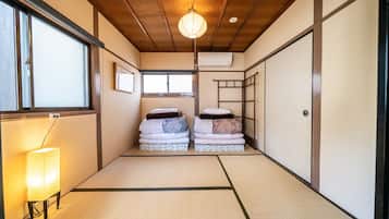 A traditional Japanese room with tatami flooring, a shoji screen, a hanging lantern, and a bed with folded bedding.