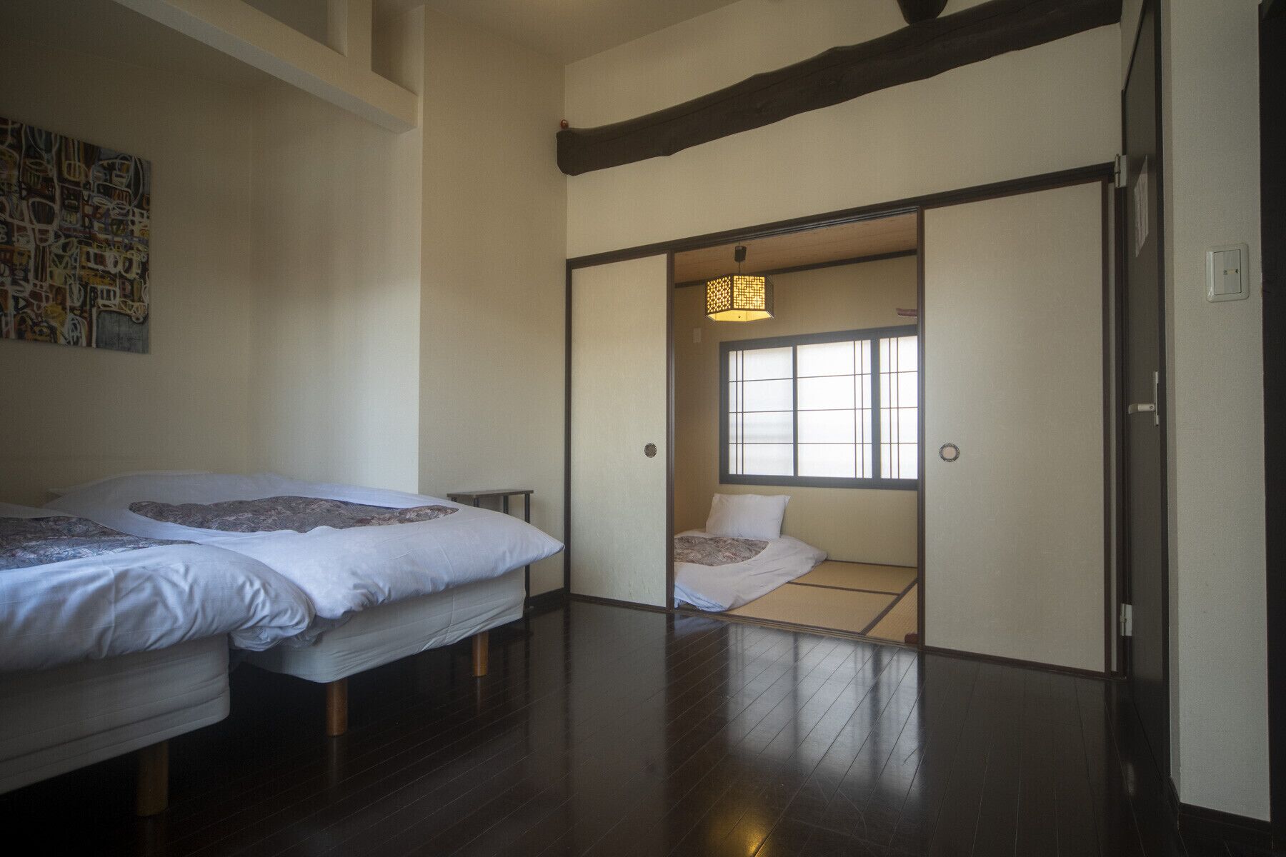 A traditional Japanese room with tatami flooring, a sliding door leading to a smaller room with a futon bed, and a shoji screen door.