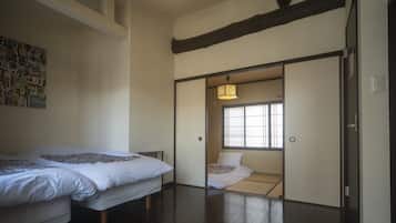 A traditional Japanese room with tatami flooring, a sliding door leading to a smaller room with a futon bed, and a shoji screen door.