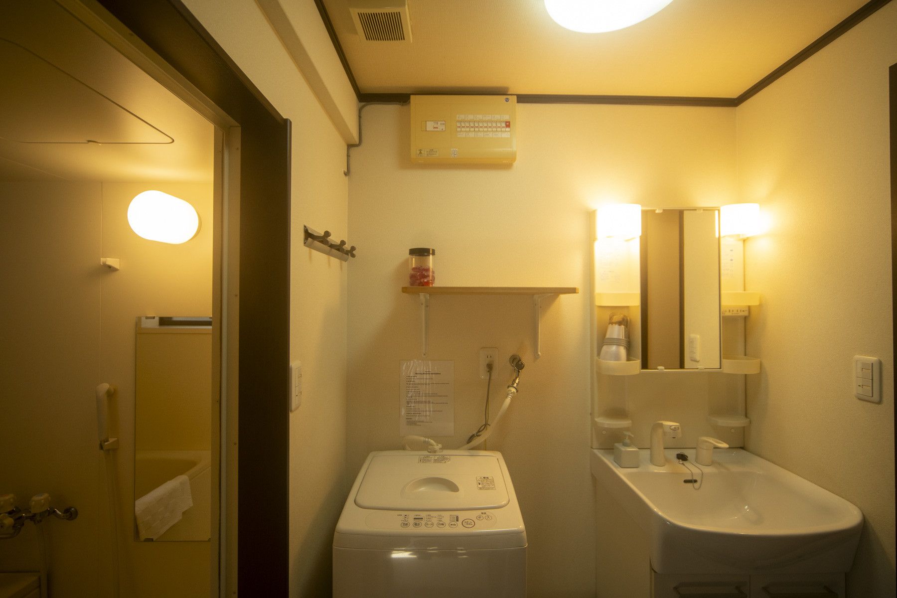 A compact hotel bathroom with a washing machine, a sink, and a mirror.