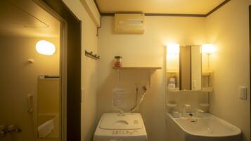 A compact hotel bathroom with a washing machine, a sink, and a mirror.