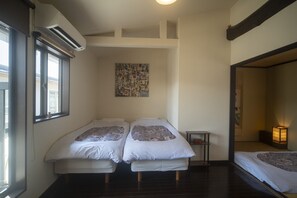 A room with two beds, a small table, a wall-mounted air conditioner, and a window. - Gojo Machiya - Traditional & comfortable Kyoto Machiya (Kyoto)