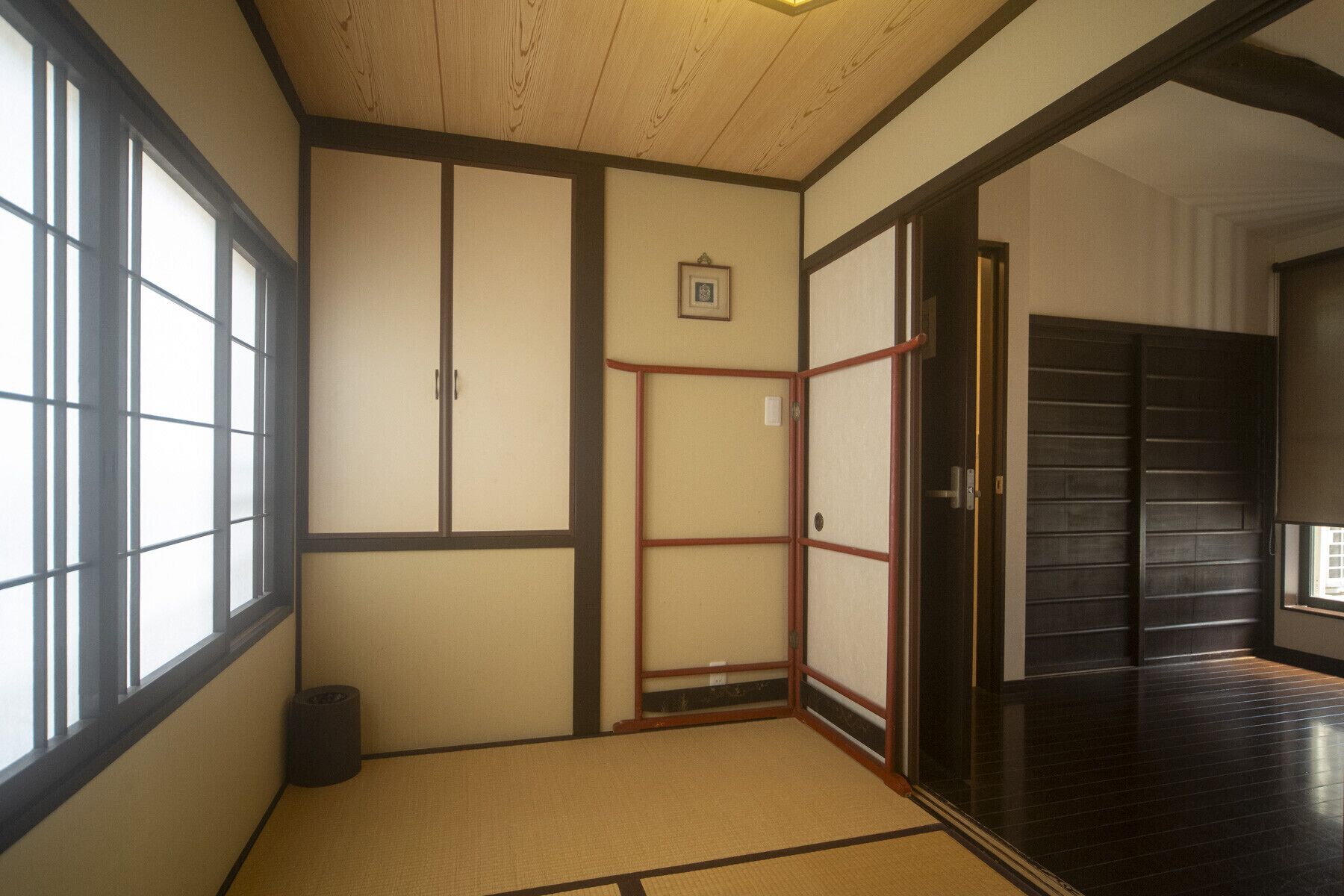 A traditional Japanese room with tatami flooring, sliding doors, and a dark wooden floor.