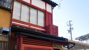 A traditional Japanese house with a red gate, a tiled roof, and a wooden balcony.