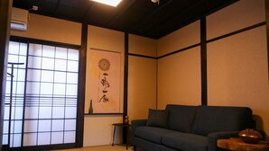 A traditional Japanese room with tatami flooring, a low dark-colored sofa, a small wooden table, and a decorative wall hanging.