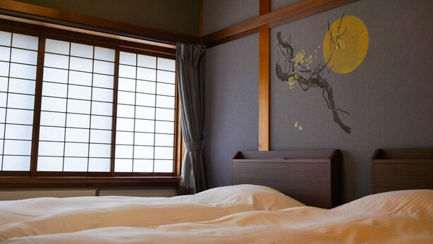 A traditional Japanese-style room with tatami flooring, a low wooden bed, a shoji screen window, and a wall-mounted artwork.