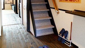 A staircase with a wooden handrail, a wall-mounted shoe rack, and a pair of slippers on the floor.