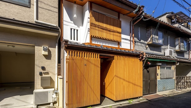 Une maison traditionnelle japonaise, dotée d’une porte en bois, d’une petite dépendance attenante et d’un climatiseur visible.