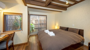Une chambre avec un grand lit, un plancher en bois, un bureau avec des chaises et une fenêtre donnant sur un paysage verdoyant.