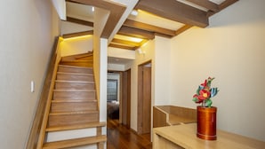Un escalier en bois au design moderne, menant à une chambre à coucher où se trouvent un lit en bois et une table de chevet agrémentée d’un vase de fleurs.