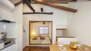 Une pièce de style japonais traditionnel, avec un sol recouvert de tatamis, une table à manger en bois pour quatre personnes et un coin cuisine équipé d’appareils modernes.