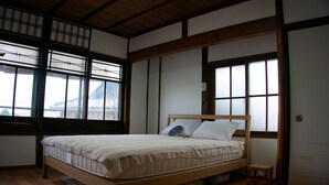 Una habitación tradicional japonesa con suelo de tatami, una cama de madera con colchón y almohadas, y una puerta corredera.