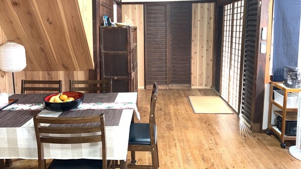 Un comedor de madera con una mesa dispuesta para dos personas, sillas, un frutero y una lámpara.