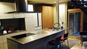 Una cocina moderna con una isla central, taburetes de bar y una escalera que lleva a un nivel superior.