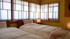 Habitación de hotel con dos camas, una mesita de noche, una lámpara y ventanas amplias con vistas.