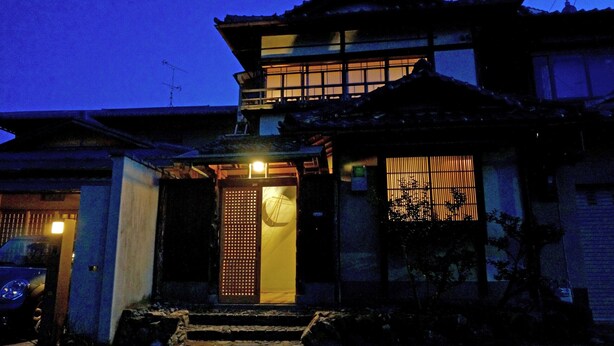 Una casa tradicional japonesa con un portón de madera, tejado de tejas y un pequeño jardín.