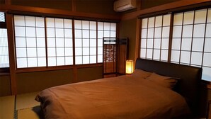 Una habitación tradicional japonesa con suelo de tatami, una cama con cabecera oscura y puertas correderas shoji.