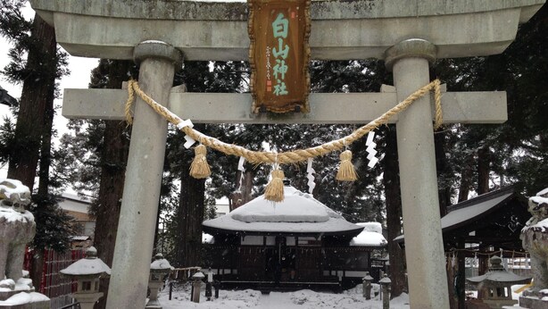 Un santuario cubierto de nieve con un tradicional torii japonés, rodeado de árboles cargados de nieve.