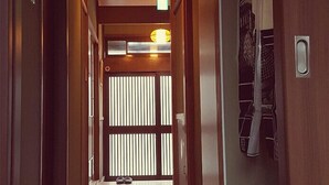 Un pasillo estrecho con paredes de madera y suelo pulido. Al final se ve una puerta con un ventanal, y una lámpara colgante sobre ella.
