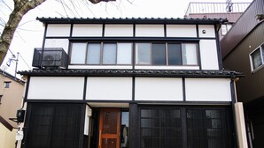 A two-story building with a traditional Japanese architectural style, featuring a wooden door and large sliding glass doors.