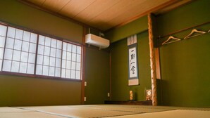 A tatami mat room with a shoji screen, tatami flooring, a hanging air conditioner, and a wall-mounted clock.