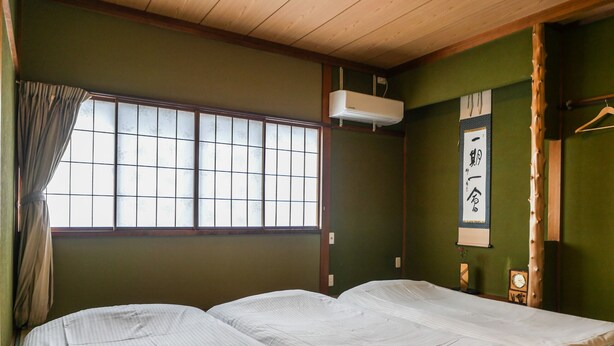 A traditional Japanese room with tatami flooring, a futon bed, a shoji screen, and a mounted air conditioner.