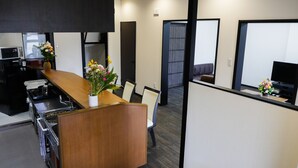 A modern hotel reception area with a wooden reception desk, a seating area with chairs, a television, and a microwave.