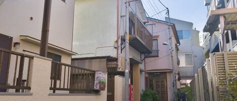 A narrow urban street with residential buildings, a bicycle, and a small garden area.