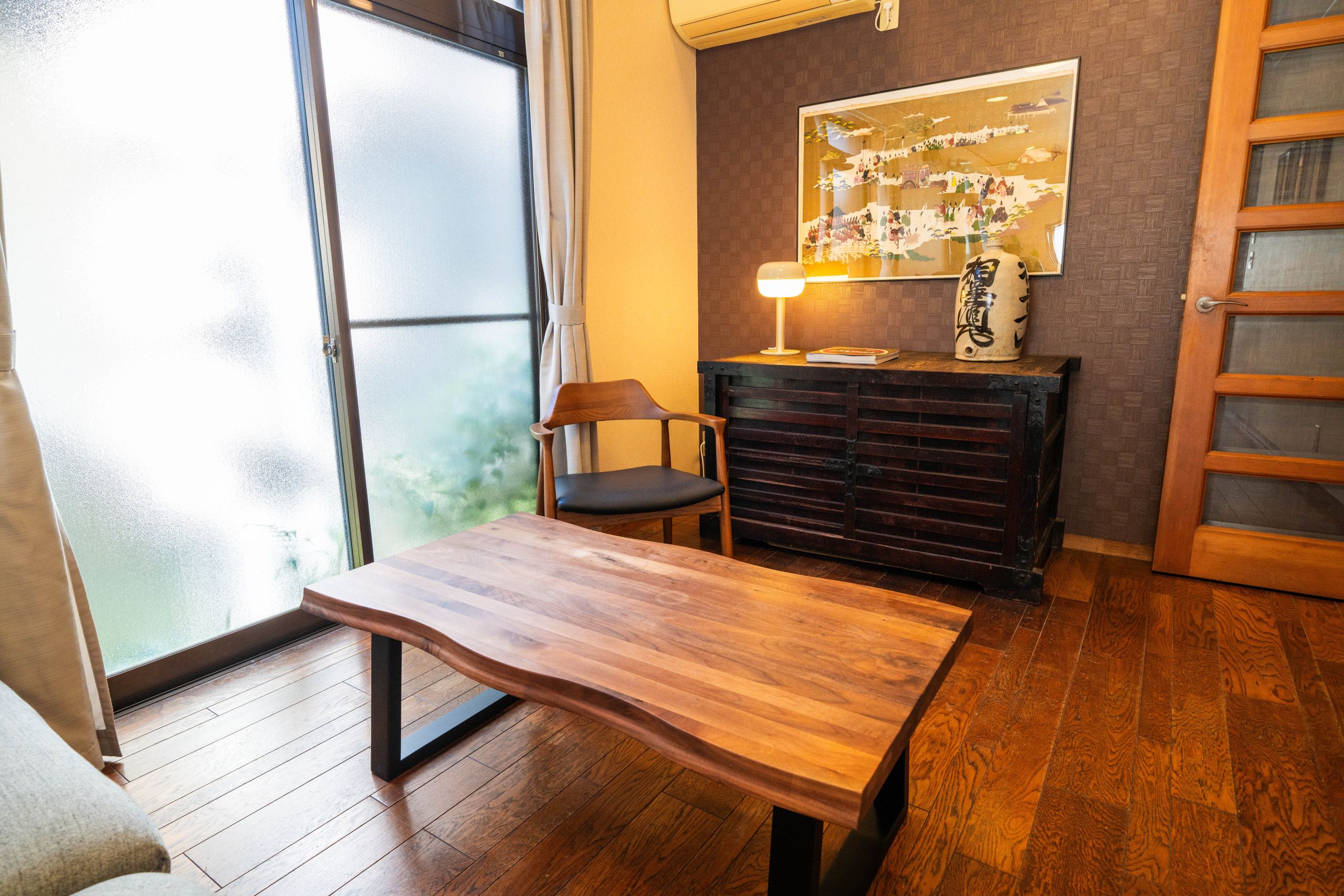 A room with a wooden table, a chair, a cabinet, and a wall-mounted lamp.