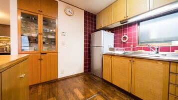 A kitchen with wooden cabinets, a refrigerator, a clock, and a tiled backsplash.