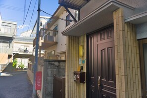 Un immeuble résidentiel doté d’une entrée sécurisée par un portail, d’une boîte aux lettres et d’un petit espace extérieur avec des marches menant à un balcon.