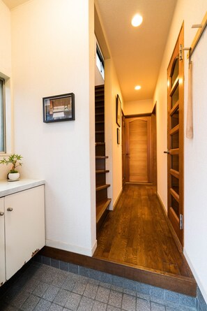 A narrow hallway with a wooden floor, a white wall with a framed picture, and a wooden door at the end.