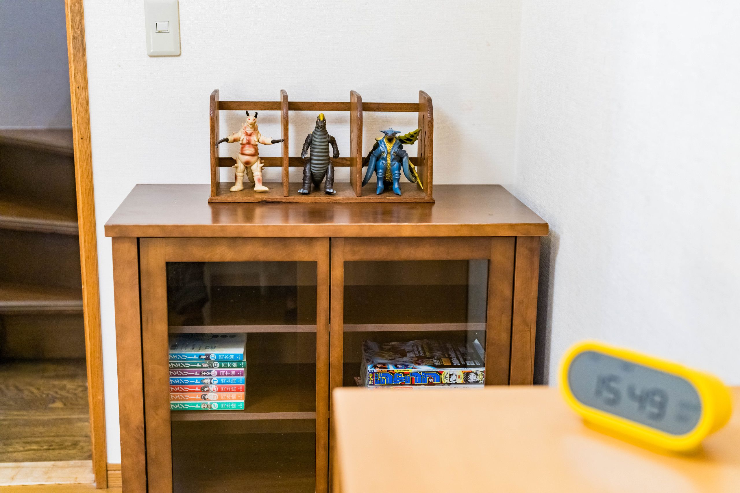 A wooden cabinet with glass doors containing figurines and manga volumes.