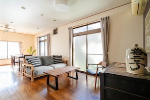 A living room with a sofa, a wooden coffee table, a dining table with chairs, and a large window with curtains. - Ikebukuro - Large comfortable house in Tokyo (Tokyo)
