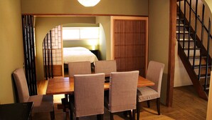 Une pièce comprenant une table à manger en bois, six chaises, un lit avec une literie blanche, une porte en bois et un escalier avec des rampes noires.