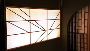 Un paravent japonais traditionnel de type « shoji », orné d’un motif géométrique et fixé au mur à l’aide d’un cadre en bois.