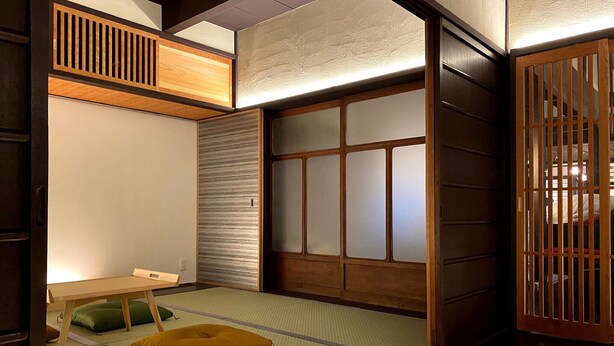 A traditional Japanese room with tatami flooring, a low table, cushions, sliding doors, and a wooden partition.