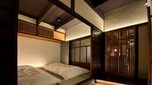 A traditional Japanese-style room with tatami flooring, a low wooden bed with a sliding door, and a small washbasin.